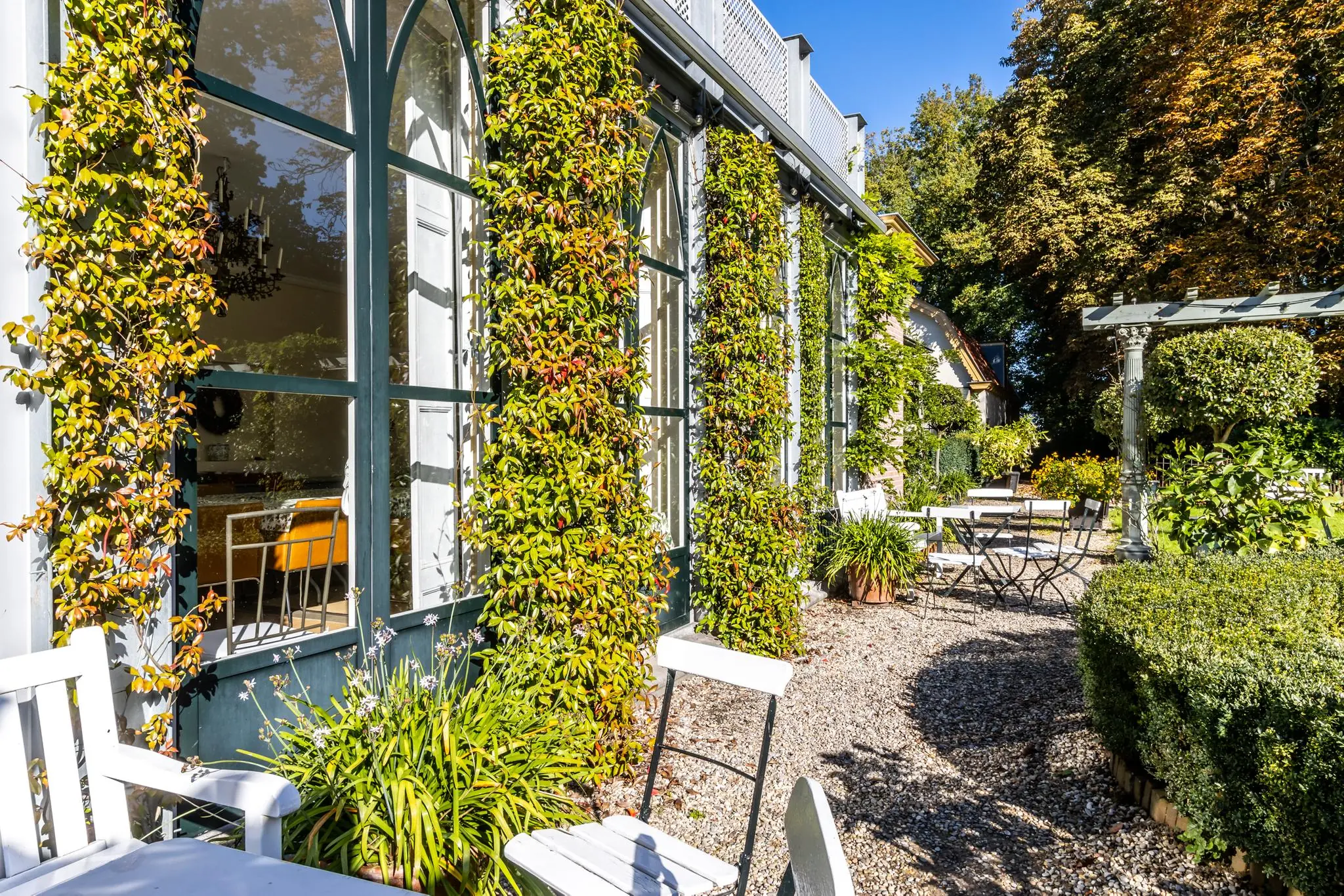 Zonnig terras met witte stoelen en tafels langs een met klimop begroeide gevel aan de Langbroekerdijk.
